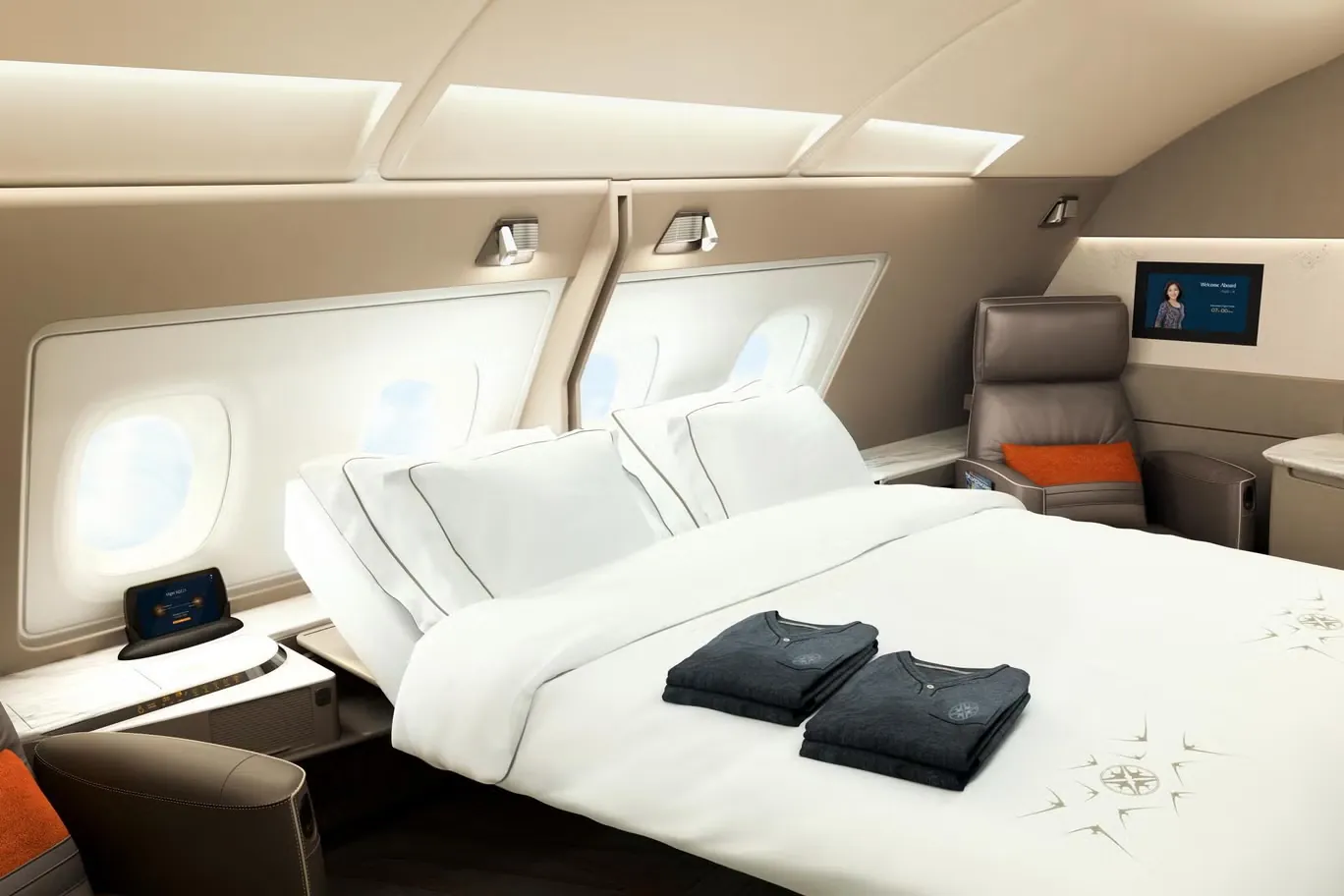 Una suite de primera clase con cama doble, ropa de cama blanca y ventanillas a bordo de un avión de fuselaje ancho